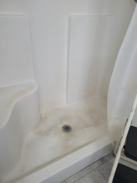 A shower pan and seat stained yellow with soap scum and grime before cleaning